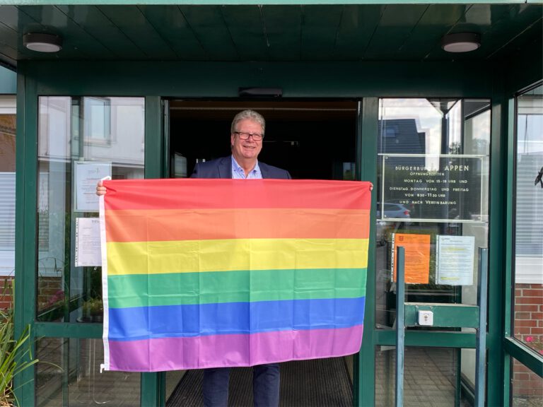 Thomas Hölck mit Regenbogenflagge vor dem Bürgerbüro Appen, Juni 2024